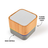 A square Bluetooth speaker with a bamboo exterior, silver mesh top, and colored music control buttons at the base.