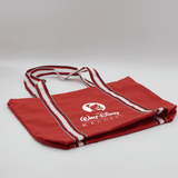 A red canvas tote bag with white striped handles and a logo on the front.