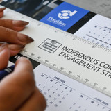 A ruler featuring a light colour with text, being held above a calendar on a table surface.