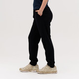 Black track pants displayed on a person, featuring side pockets and a casual fit, paired with beige athletic shoes.