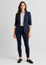 A woman stands in a navy blazer and white blouse, wearing navy high-rise pull-on leggings and black shoes.