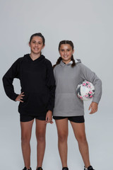 Two girls wearing hoodies, one black and one grey, stand together. One girl holds a patterned ball.