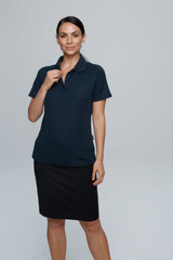 A woman poses in a navy blue polo shirt paired with a black skirt. The shirt features a logo.