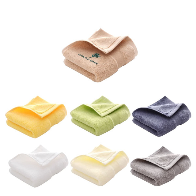 A stack of embroidered cotton hand towels in shades of beige, yellow, green, blue, grey, and white, featuring a logo.