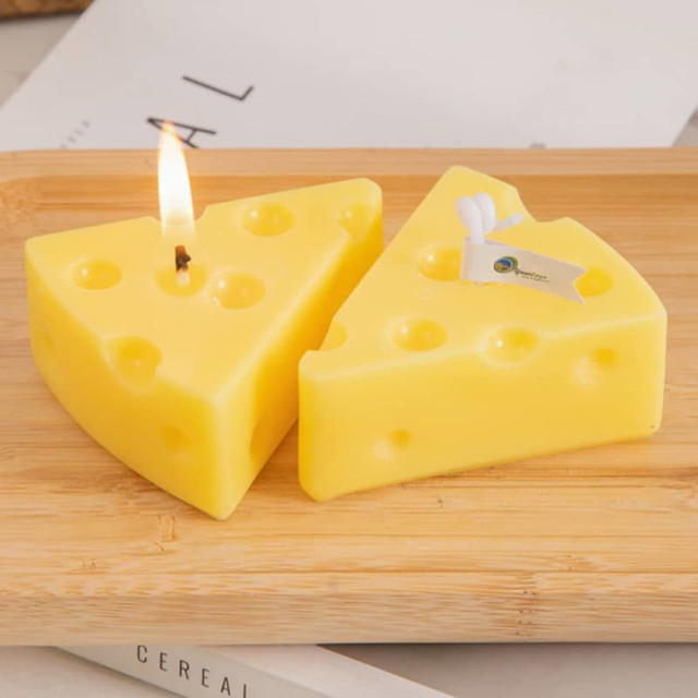Triangle-shaped candles in yellow, resembling cheese, displayed on a wooden surface. One candle is lit.