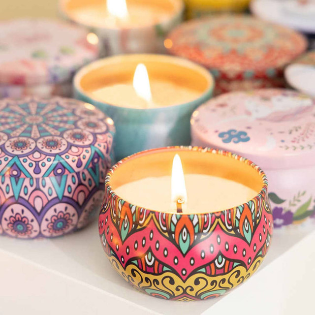 A collection of colourful tin candles with intricate designs and lit wicks, arranged on a white surface.