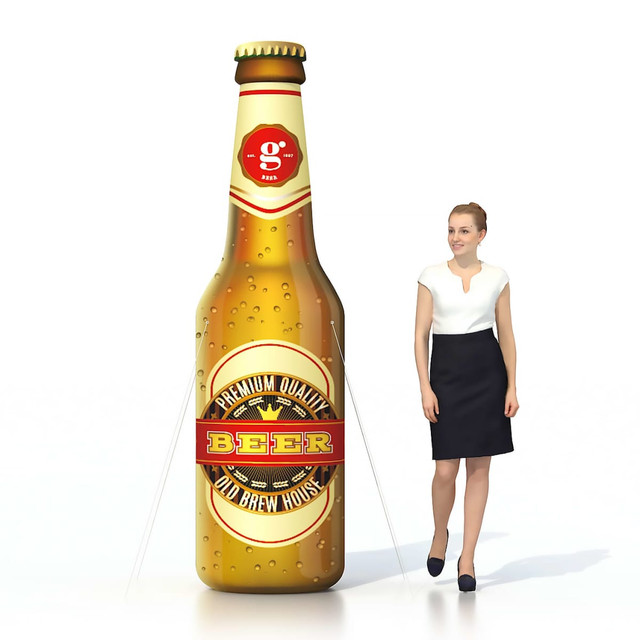 An inflatable beer bottle in brown with a label and a woman in a black skirt and white top beside it.