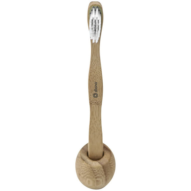 A bamboo toothbrush in natural tan colour, with soft bristles, resting in a round holder. It features a logo.