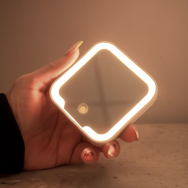 A compact mirror with an LED light in a square shape, held in a hand, featuring a sleek design.