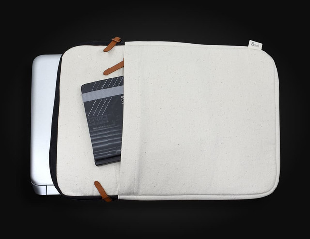 A cream-coloured laptop sleeve with leather accents, showing a partially open compartment and a notebook inside.