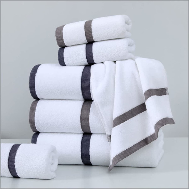 A stack of white bath towels with grey stripes, featuring both rolled and folded towels. Includes a towel with a corner draped.