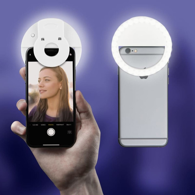 A hand holds a smartphone with a Smiley LED Selfie Light attached, featuring a circular white light and glowing ring.