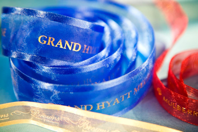 A roll of custom printed organza ribbon in blue, red, and gold, featuring different brands, with satin edges.