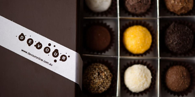 A box of assorted chocolates featuring different colours and textures, with a branded band across the front.