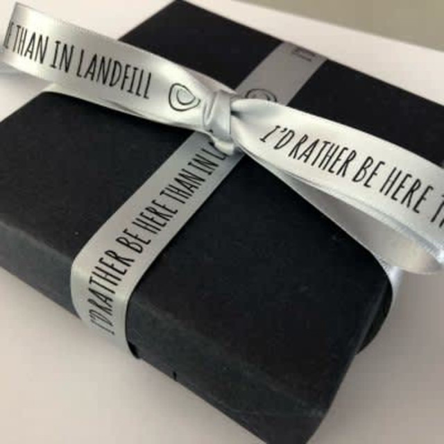 A black gift box tied with a grey satin ribbon featuring a logo and printed text.