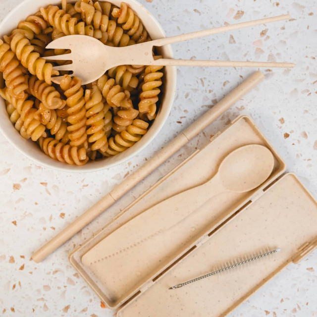 A tan Ramen Cutlery Set with a spoon, fork, and chopsticks, placed beside a bowl of rotini pasta.