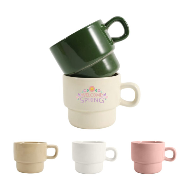 Stackable ceramic mugs in green, beige, white, and pink, featuring a decorative design on one mug and a logo.