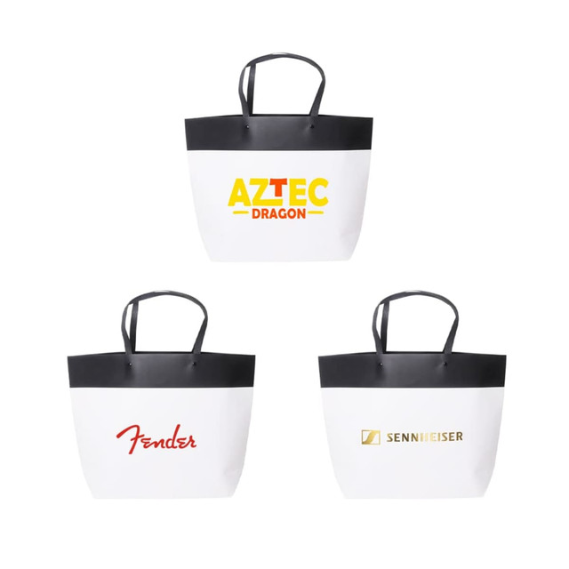 Three medium black and white boutique paper bags featuring black handles and various logos on the front.