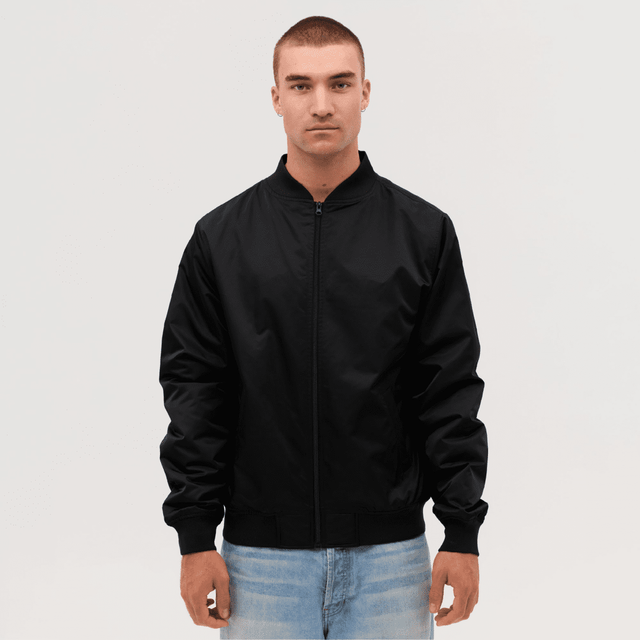 A black bomber jacket worn by a model, featuring a zip front and ribbed cuffs. The model has short hair and is standing against a neutral background.