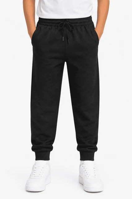 Tapered fleece kids pants in black with elastic waistband and side pockets, paired with white sneakers.