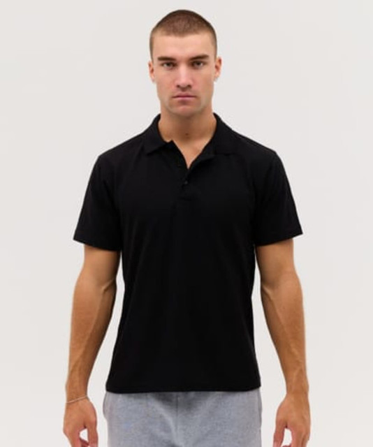 A black polo shirt displayed on a male model, featuring a collar and short sleeves. The shirt has a logo.