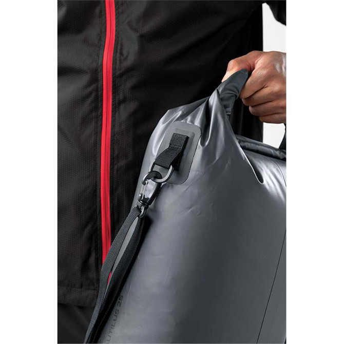 A hand holds a grey Nautilus 25 roll-top backpack, featuring a clip attachment and adjustable strap.