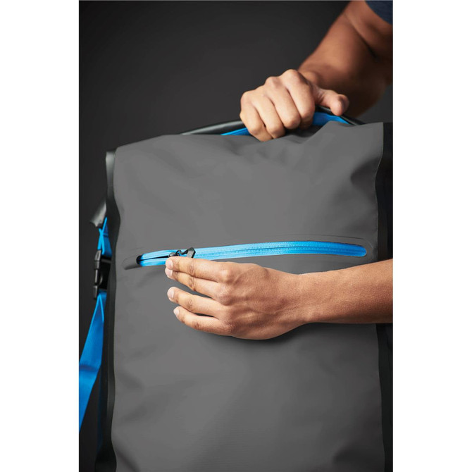 A grey backpack with blue zippers is being held, showcasing a zippered pocket on the front.