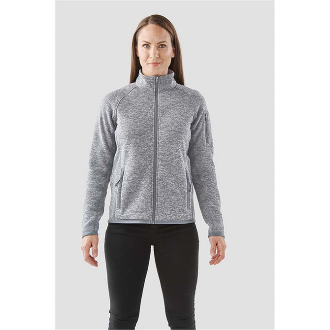 A woman is wearing a grey full zip fleece jacket with a high collar and side pockets. The jacket features a logo.