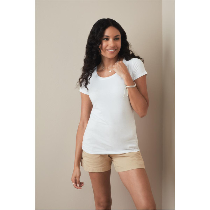 A woman models a white crew neck t-shirt paired with light brown shorts, standing against a neutral background.