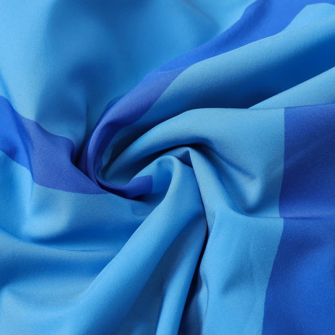 A close-up of lightweight, knee-length swim shorts made from polyester and spandex in shades of blue, featuring a logo.
