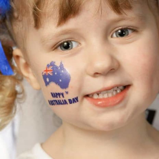 A child with a temporary tattoo of Australia featuring a small flag on their cheek, smiling cheerfully.
