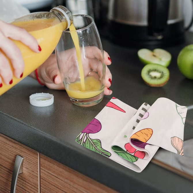 A tea towel with a colourful vegetable design, featuring shades of red, green, and purple, is placed near a drink being poured.