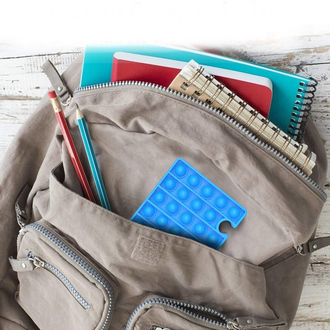 A blue Puzzle Shape Pop It Fidget Toy tucked inside a backpack, alongside notebooks and pens.
