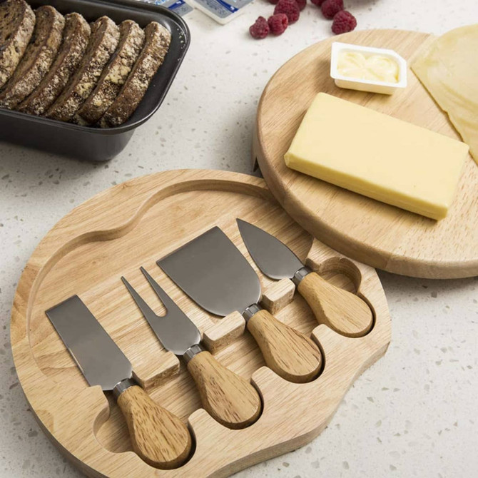 A cheese board set featuring a wooden board, four stainless steel knives with wooden handles, cheese, and crackers.