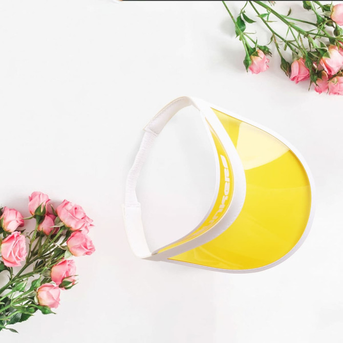 A yellow PVC sunscreen hat with a white band, placed against a backdrop of pink roses. It features a logo on the side.