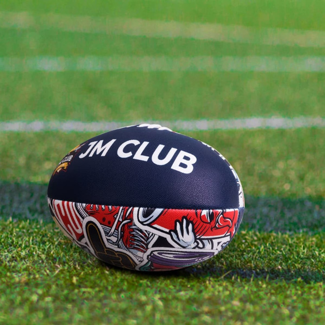 A training AFL ball in dark blue with vibrant red designs, featuring a logo, resting on a grassy field.