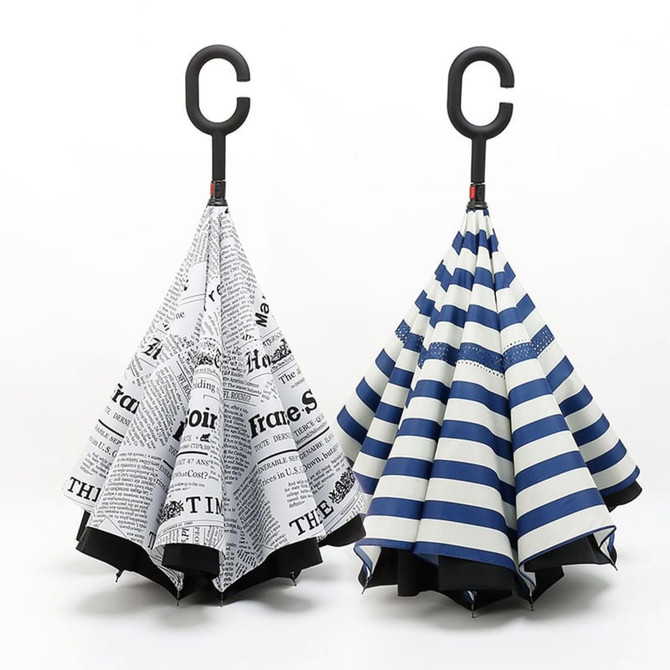 A reversible folding umbrella featuring black and white newspaper print on one side and navy stripes on the other, with a curved handle.