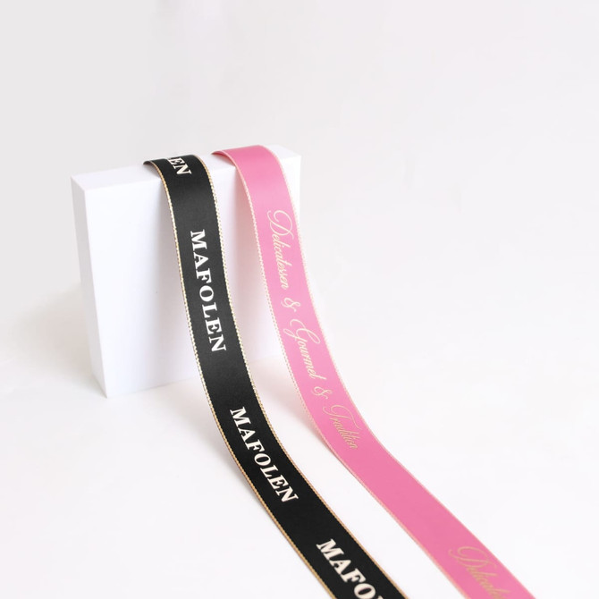 Two ribbons in black and pink, featuring gold-edged details and logos, arranged against a plain white background.