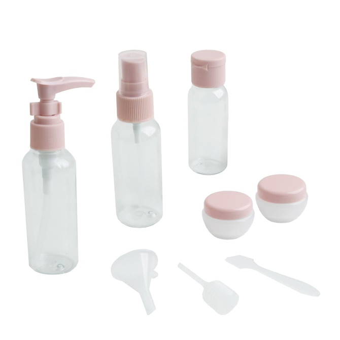 A set of clear toiletry bottles and jars with pink lids, including a pump, spray, and containers with a funnel and spatula.