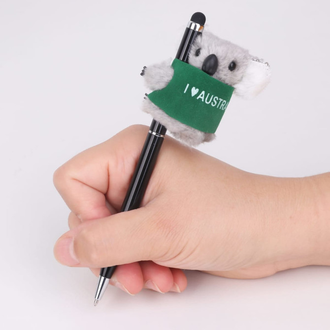A hand holding a black pen topped with a grey koala plush toy wearing a green "I ♥ AUSTRALIA" band.
