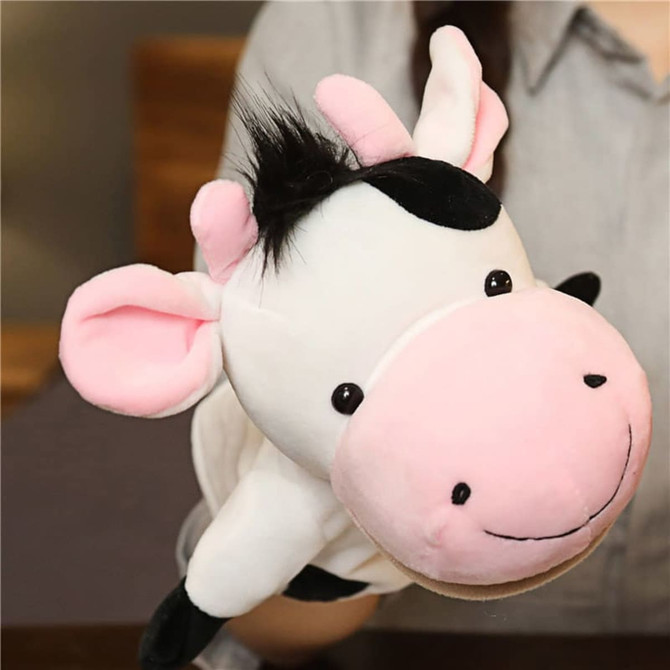 A cow hand puppet in black and white, with pink ears and a round face, held by a person.