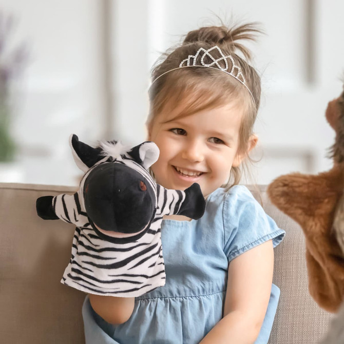 A zebra hand puppet in black and white is being held by a smiling child wearing a blue dress.