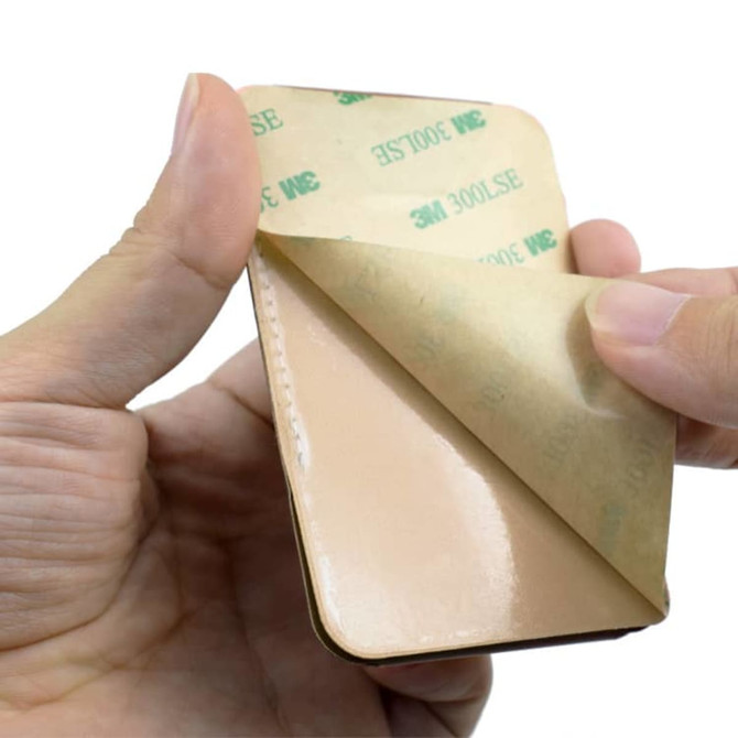 A PU phone stand card holder in tan colour being held, with an adhesive backing partially peeled away.