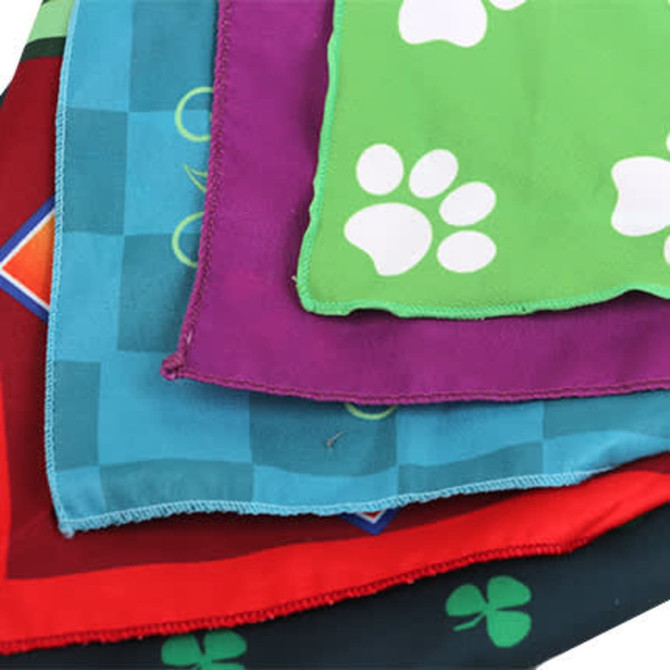 A stack of triangle pet bandanas in red, green, purple, and turquoise, featuring patterned designs and a logo.