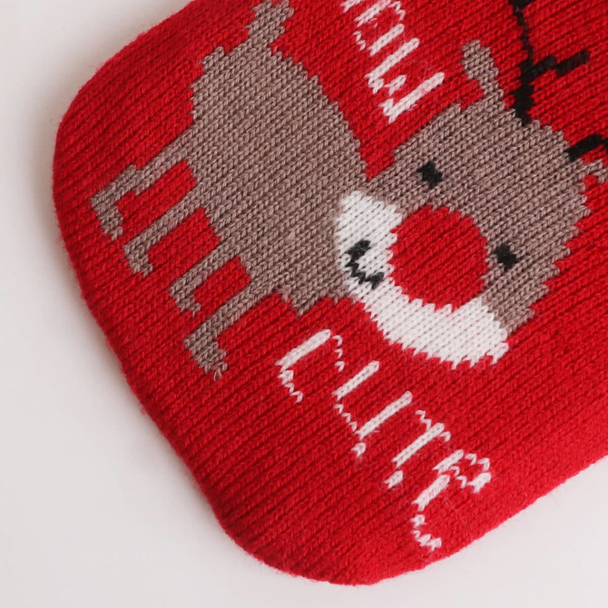 A red knitted cover for a hot water bottle featuring a reindeer design with white and grey details.
