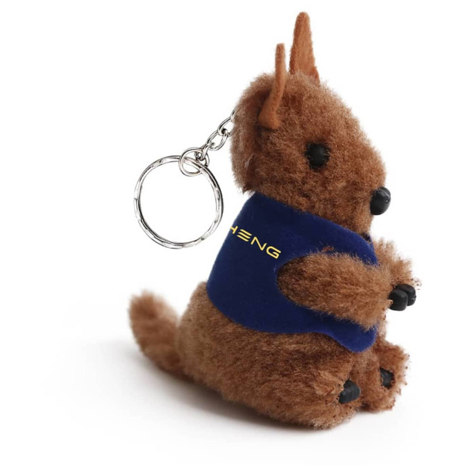 A brown plush kangaroo toy with a keychain, featuring a blue vest and black accents, and a small branding logo.