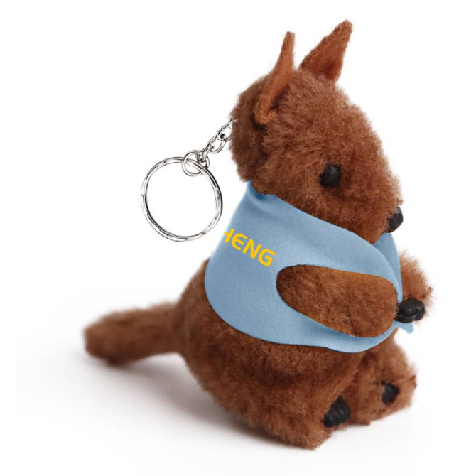 A brown kangaroo plush toy with a blue vest and a keychain. The toy is seated and has a soft texture.