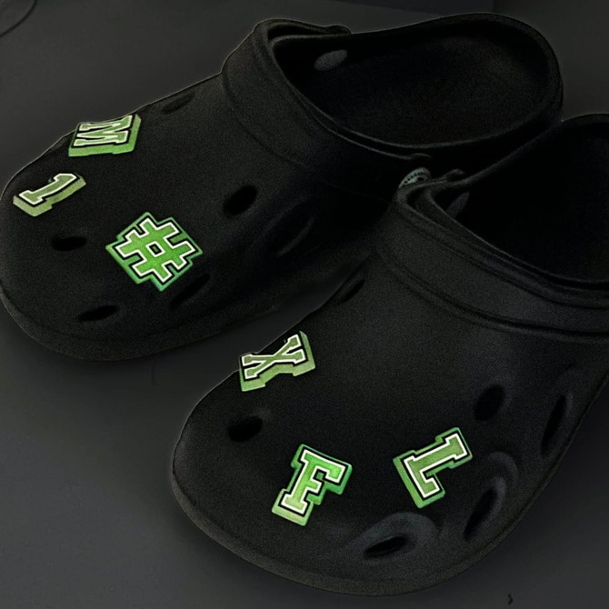 Black clog shoes adorned with green glowing charm letters and symbols for a fun and novelty look.