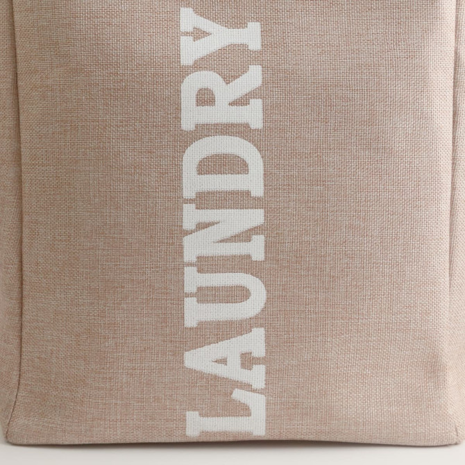 A laundry basket in a beige fabric with white lettering, featuring a sturdy handle and a simple design.