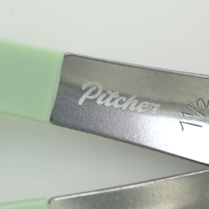 A set of measuring spoons with green handles and metal heads, featuring an engraved logo on the metal.